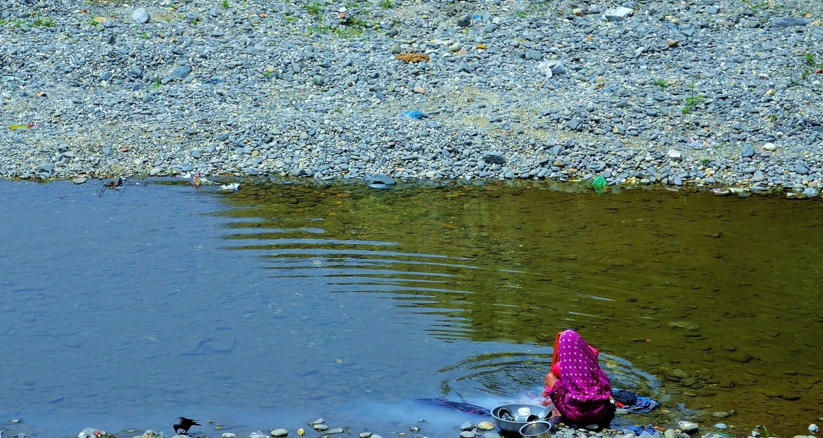 Indian woman washes vessels and clothes in a stream