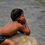 A boy relaxes on a rock in a river