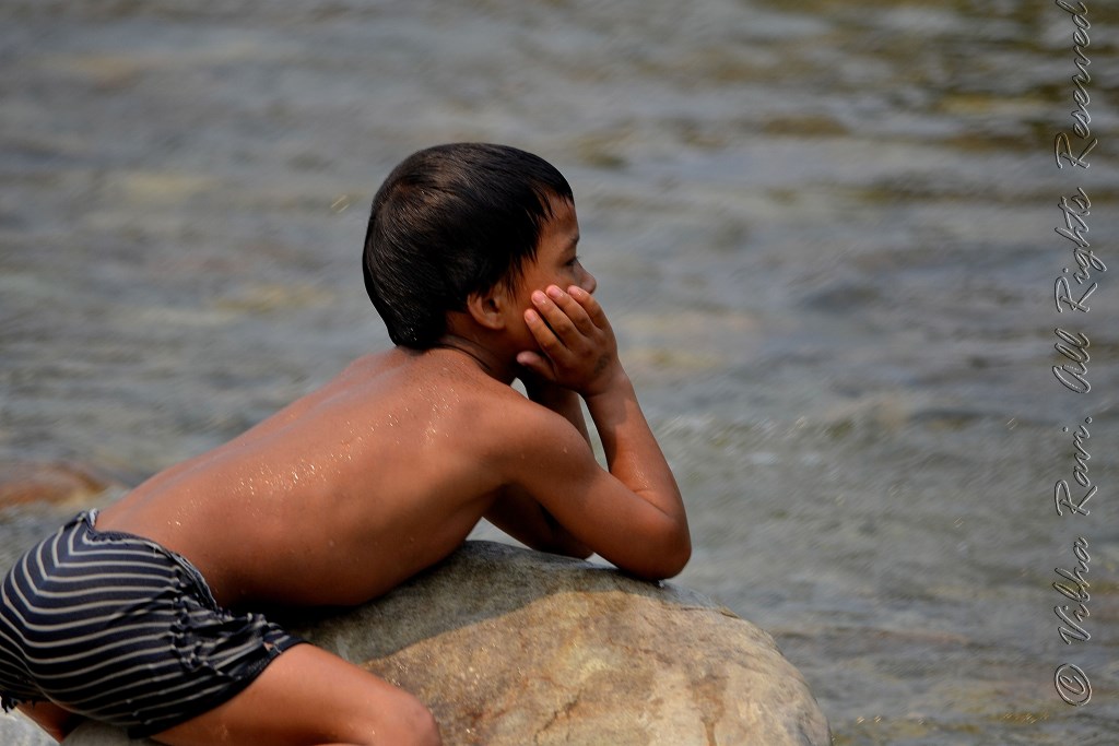 A boy relaxes on a rock in a river